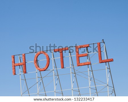 Red neon hotel sign against blue sky.