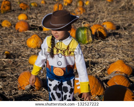 Little girl in Halloween costume looking for big pumpkin on pumpkin patch.
