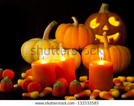 Lit orange candles with small pumpkins and jack-o\'-lantern on black background.