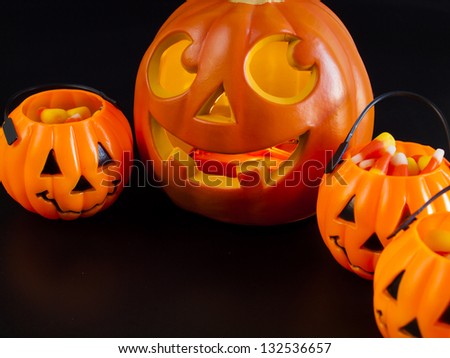 Lit jack-o\'-lantern with Halloween pumpkin bags on black background.