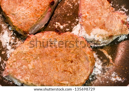 Cooking beef liver covered in flour on a frying pan.