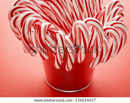 White and red peppermint candy canes in bucket on red background.
