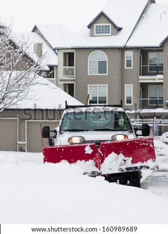 A large pickup truck with a snow plow clearing a dryway in aparment complex.