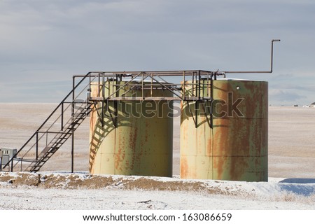 Rusted industrial storage tanks in winter landscape.