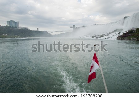 The Canadian flag flaps from the back of a tour boat with Niagara Falls in the background.