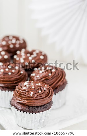 Gourmet chocolate cupcakes decorated with silver balls on chocolate icing.