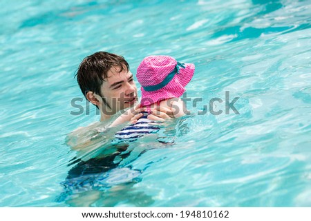 Family with cute baby girl faving fun in outdoor swimming pool on hot summer day.