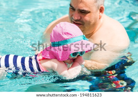 Family with cute baby girl faving fun in outdoor swimming pool on hot summer day.