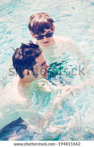 Brothers faving fun in outdoor swimming pool on hot summer day.