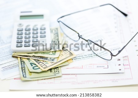 Calculating income tax return with folded cash on a table.