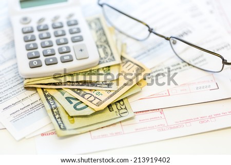 Calculating income tax return with folded cash on a table.