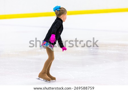 Young figure skater practicing at indoor skating rink.