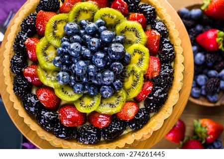Fresh fruit tart on cake stand on wood table.