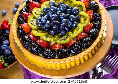 Fresh fruit tart on cake stand on wood table.