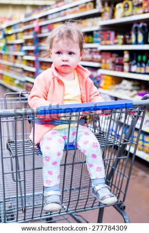 Cute toddler girl sitting in shopping cart at the grocery store.