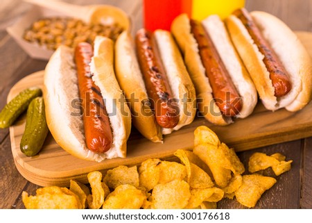 Grilled hot dogs on a white hot dog buns with chips and baked beans on the side.