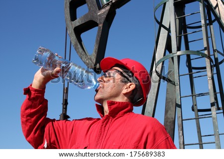 Thirsty Oil Industry Worker.Thirsty oil worker drinking water from bottle in front of the pump jack.