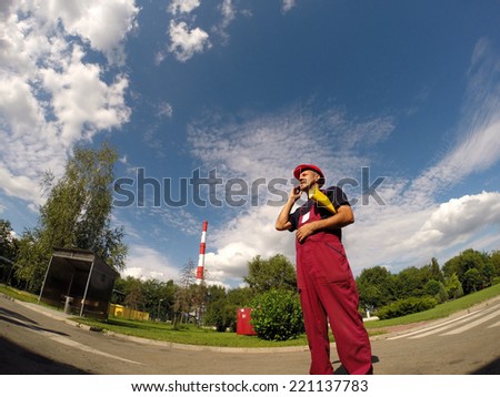 Industrial Worker With Red Hard Hat Using Cell Phone.Industrial worker with cell phone against a blue sky with white clouds.
