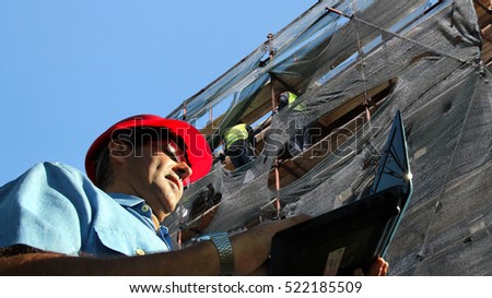 Architect or Engineer With Laptop Computer on a Building Site / Architect or Engineer typing on laptop computer and two workers on scaffolding in the background