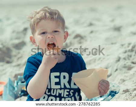 hungry kid with open mouth eating salty fat chips or junk food on the beach
