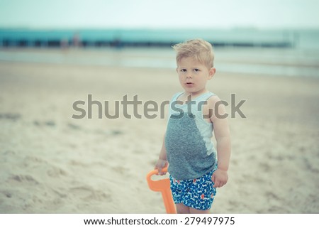little boy on the beach in a wet shirt looking at the camera