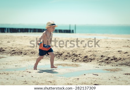 little boy surf dude is running through the sand and water on the beach