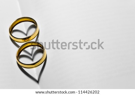 Two wedding rings on top of the blank pages that form two hearts with their shadows
