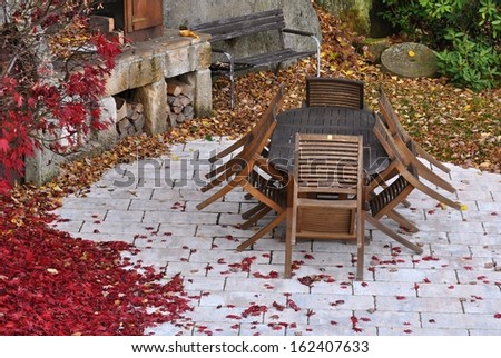 Autumn garden with old wooden furniture covered by leaves