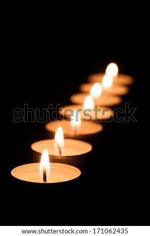 Many of burning tea light candles on a black background