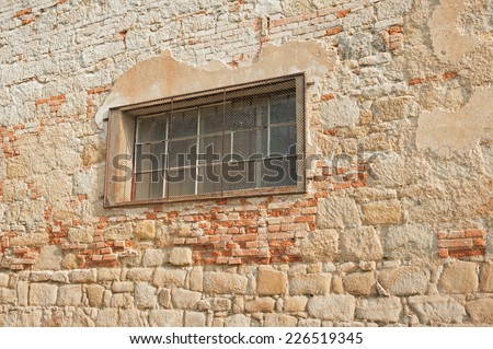 Old stone wall with fallen plaster and window with bars