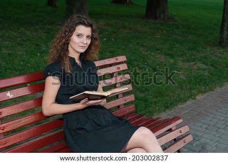 Beautiful young girl in evening reading book on park bench