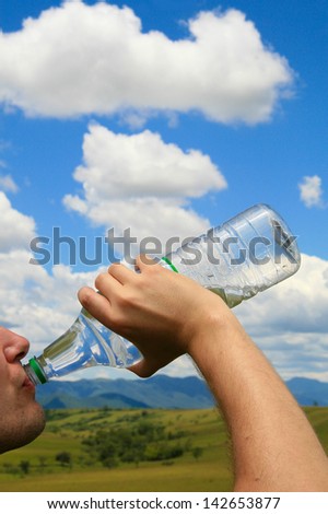 Man drinking water out of polyethylene plastic bottle in front of a blue sky