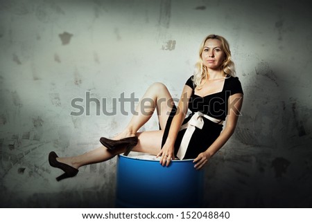 White girl with an elegant black dress sitting on a barrel in a grunge environment