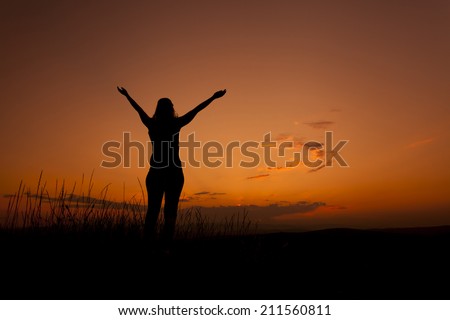 Woman silhouette rising hands in the sunset sky as a worship