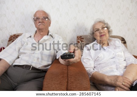 Senior couple watching tv. The man uses the remote to change channels