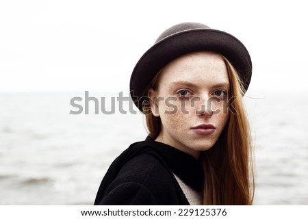 outdoor portrait of young girl with freckles and red hair in a black hat