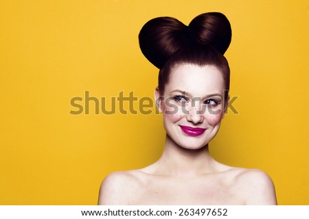 Beauty Smiling Teenager Model Girl. Beautiful Joyful teen girl with freckles, funny hairstyle and bright makeup. Isolated on a yellow background