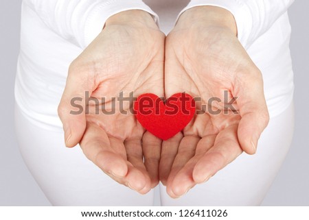 Women caring for a fabric heart with both hands on a gray background.