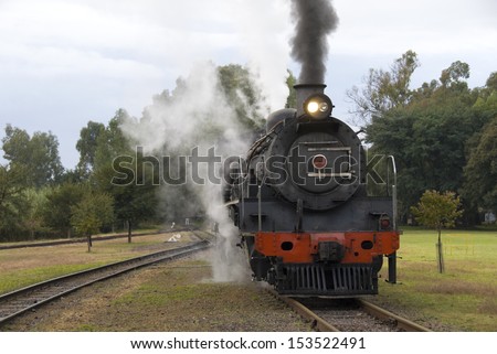 Steam train traveling along the railway line with steam bellowing out the sides and the top
