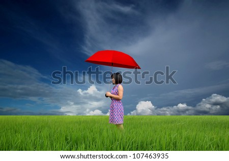 young woman with red umbrella in a green field under rain