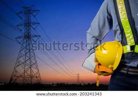 Engineer holding a yellow helmet for the safety of workers on the background. Silhouette transmission towers on the background of the evening sun.
