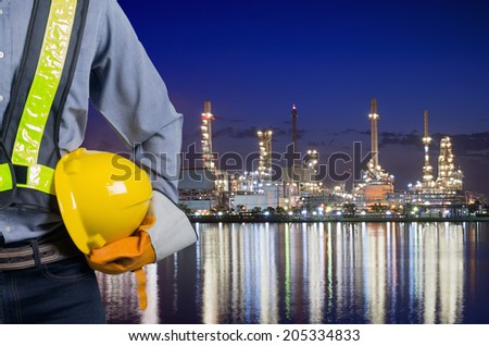 Engineer holding a yellow helmet for the safety of workers on the background oil refinery. Beautiful sky at dawn
