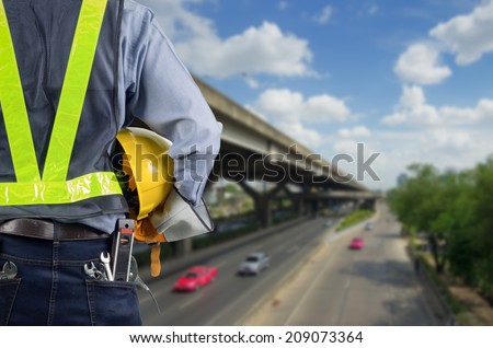 Engineer holding a yellow helmet for the safety of the workers, with expressway as a backdrop