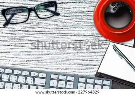 Work desk with notebook, pen, glasses, Red coffee cup, and keyboards.