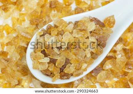 Rock sugar from sugar cane on a white spoon.