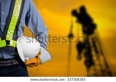 Engineer holding a white helmet for the safety of construction workers on a background crane Silhouette sunset.