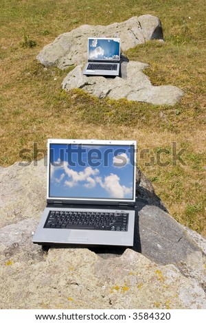 two laptops on big stones with blue sky reflection on the screens