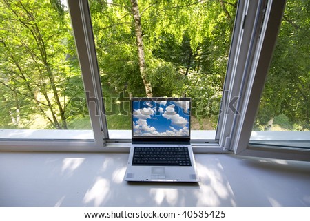 Opened plastic window in room with view to green trees and portable computer