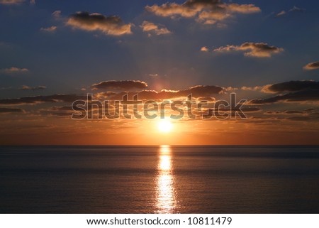 The sun sets against a clean ocean horizon in the Caribbean.