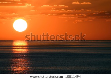 The sun sets against a clean ocean horizon in the Caribbean.